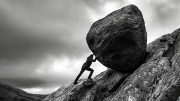 man pushing rock up a mountain 